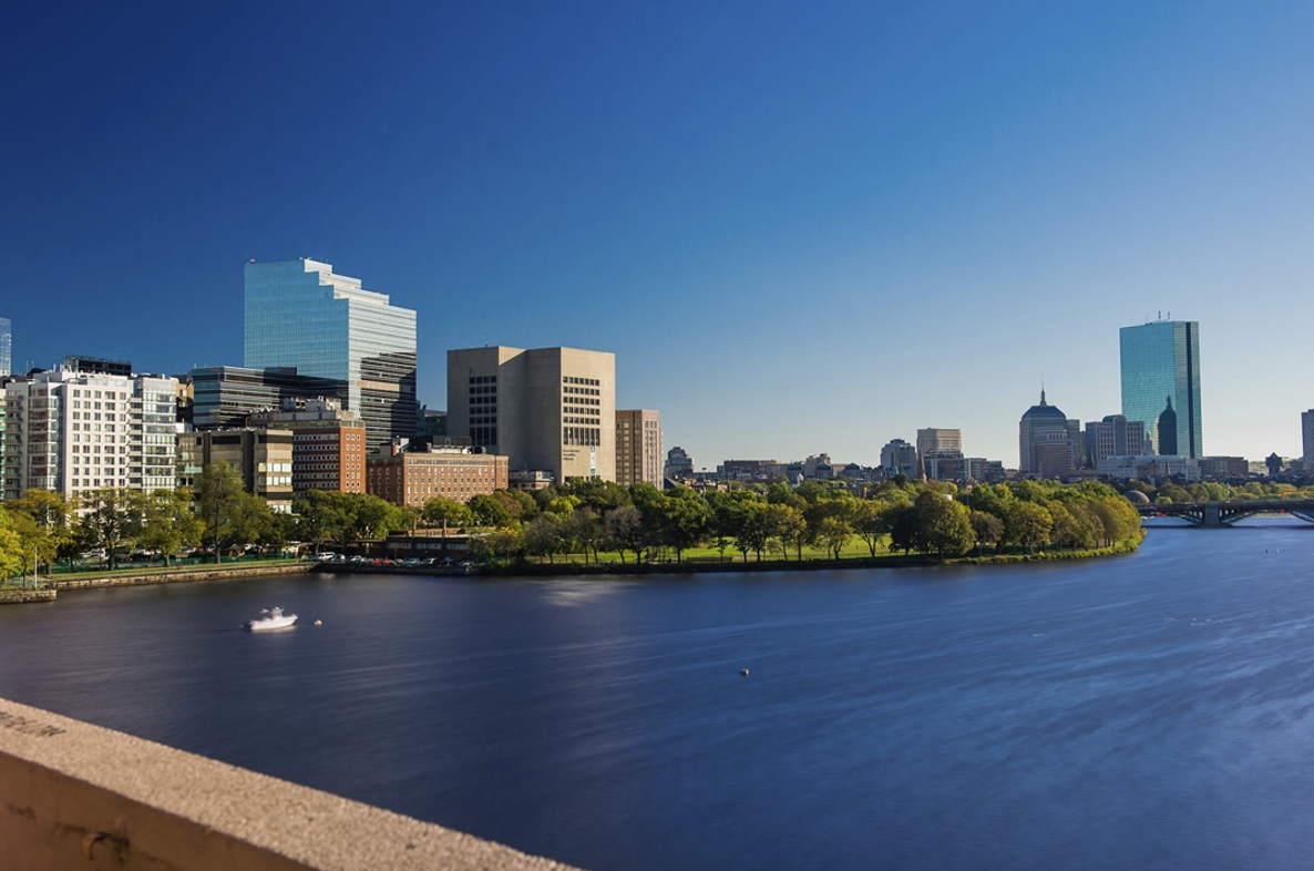 Boston skyline seen across the Charles River on a sunny day with boats on the water.